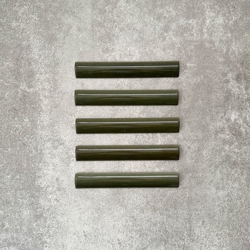 Flatlay von Zellige Botanisches Grün Bordürenfliese Keramik-Abschlussfliesen im marokkanischen Stil im Format 3 × 20 cm, in tiefen botanischen Grüntönen. Mit glatt abgerundetem Profil und glänzender Glasur auf einem strukturierten grauen Hintergrund arrangiert, um den handgefertigten Zellige-Effekt und das dekorative Abschlussprofil hervorzuheben.