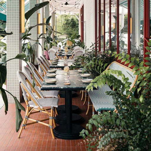 Restaurantterrasse mit Atlas Terrakotta Mini Brick Matt Wand- und Bodenfliesen im Format 5 × 15 cm, kombiniert mit Sitzmöbeln aus Rattan, üppigem Grün und gestreiften Markisen für einen warmen, mediterran inspirierten Außenbereich.