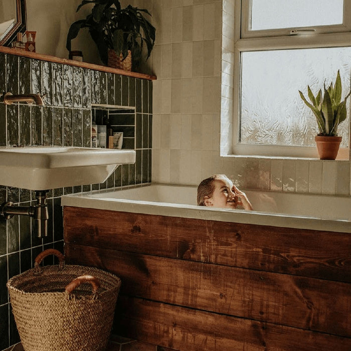 Badezimmer mit Zellige Botanisches Grün Ziegel Keramik-Wandfliesen im marokkanischen Stil im Format 6,5 × 20 cm, in tiefen Grüntönen. Vertikal im Ziegelverband rund um eine eingebaute Badewanne verlegt und kombiniert mit warmer Holzverkleidung, weißer Keramik und botanischen Akzenten entsteht ein reiches, charaktervolles Finish mit Zellige-Effekt.