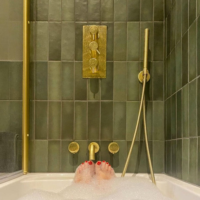 Badezimmer mit Zellige Malachitgrün Matt Keramik-Riemchenfliesen im marokkanischen Stil im Format 6,5 × 20 cm, rund um Badewanne und Dusche an den Wänden verlegt. In Kombination mit gebürsteten Messingarmaturen, einem Waschtisch aus Holz und einem Steinwaschbecken entsteht ein warmes, spa-ähnliches Ambiente.