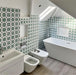 Badezimmerinterieur mit Agadir Grün Fliesen im marokkanischen Stil im Format 20 × 20 cm aus Feinsteinzeug, eingesetzt als Wandfliesen mit sich wiederholendem geometrischem Sternmuster in Grün und Weiß. Kombiniert mit freistehender Badewanne, moderner Sanitärausstattung und einer hellen, luftigen Raumgestaltung.