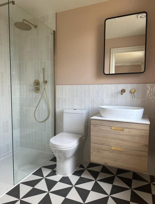 Badezimmer mit Harlekin Dreieck Schwarz & Weiß 20 × 20 cm Feinsteinzeug-Bodenfliesen in einem markanten schwarz-weißen geometrischen Muster, kombiniert mit weißen Wandfliesen, roséfarbenen Wänden und einem Waschtisch aus Holz für einen modernen Statement-Badezimmerboden.