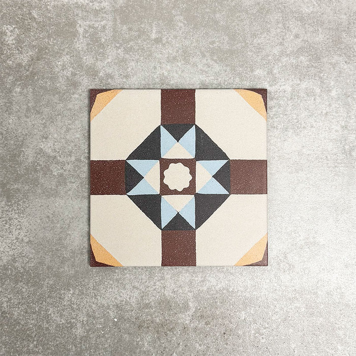 Einzelne Berlin Kreuz Feinsteinzeugfliese im Format 20 × 20 cm im viktorianisch-marokkanisch inspirierten Stil in einer Produktszene. Gezeigt wird ein geometrisches Sternmuster in Burgunder-, sanften Blau-, Anthrazit- und Cremetönen, inspiriert von traditionellen dekorativen Bodenfliesen.