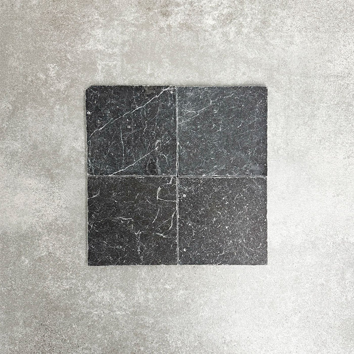 Vier Fayrouz Black Naturmarmorfliesen im Format 15,2 × 15,2 cm mit getrommelter Oberfläche, gemeinsam arrangiert. Sichtbar werden tiefe Anthrazittöne, natürliche Maserungen und feine Oberflächenvariationen vor einem neutralen, strukturierten Hintergrund.