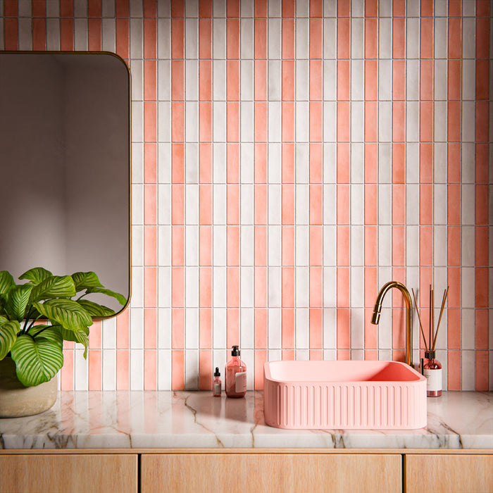 Waschtischbereich im Badezimmer mit Benomar Ziegelfliesen im marokkanischen Stil in sanften Rosé- und Elfenbeintönen, vertikal als Statement-Wand verlegt und kombiniert mit einem geriffelten rosafarbenen Waschbecken, einer Armatur in gebürstetem Messing, einer Marmoroberfläche und Pflanzen.