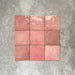Flatlay von Zellige Rosa Quadrat Keramikfliesen im marokkanischen Stil im Format 13,2 × 13,2 cm, in sanften Blush-, Altrosa- und warmen Rosétönen. Feine Farbvariation und leicht unregelmäßige Kanten werden im schlichten Raster auf strukturiertem grauem Hintergrund präsentiert und unterstreichen die handgefertigte Zellige-Optik.
