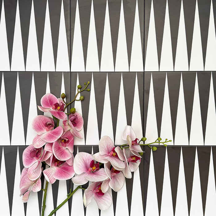 Schwarz-weiße Bodenfliese im Format 20x20 cm mit ausdrucksstarkem, geometrischem Muster im Backgammon-Stil. Markante Dreiecksformen treffen auf einen strukturierten grauen Hintergrund und schaffen eine klare, grafische Wirkung.
