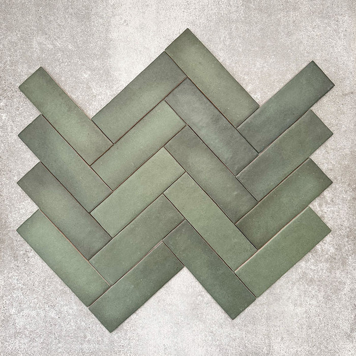 Flatlay von Zellige Malachitgrün Matt Keramik-Riemchenfliesen im marokkanischen Stil im Format 6,5 × 20 cm, im Fischgrätmuster angeordnet. Die matte Oberfläche, dezente Tonabstufungen und die handwerkliche Optik stehen im Fokus.