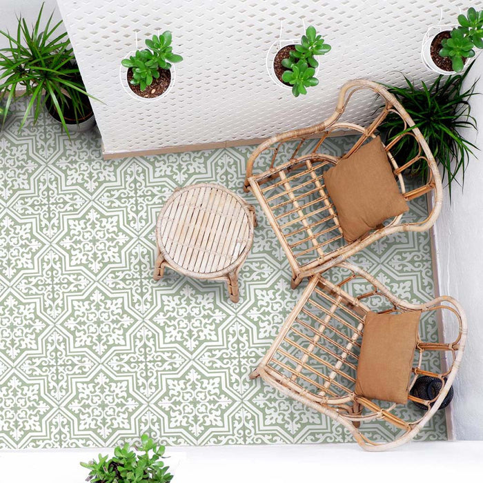 Außenbereich mit Sitzplatz, ausgestattet mit Rattanstühlen, einem kleinen runden Tisch und hängenden Pflanzen, gestaltet mit Berlin Trondite Grün Bodenfliesen im Format 20 × 20 cm im viktorianisch-marokkanisch inspirierten Stil. Gezeigt wird ein frisches Muster in Salbei und Weiß.