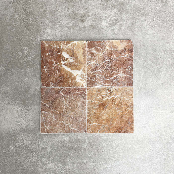 Vier Fayrouz Rosso 15,2 × 15,2 cm Naturmarmorfliesen mit getrommelter Oberfläche nebeneinander angeordnet, die warmen Rottöne, markante Maserung und natürliche Variation vor einem neutralen, strukturierten Hintergrund zeigen.