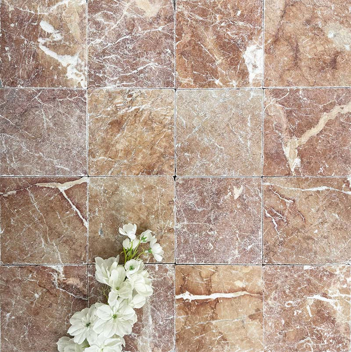 Flatlay mit Fayrouz Rosso 15,2 × 15,2 cm Naturmarmorfliesen mit getrommelter Oberfläche in warmen Rottönen mit natürlicher Maserung und Oberflächenvariation, kombiniert mit zarten weißen Blumen für einen sanften Kontrast.