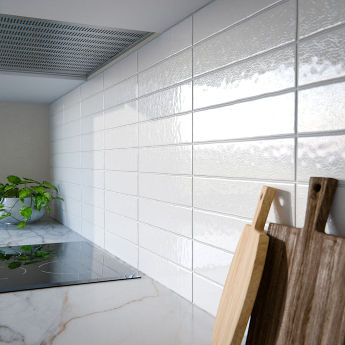 Moderne Küche mit Bora Bora Ziegel Weißer Sand Keramik-Wandfliesen im schlanken Riemchenformat 6,5 × 32,8 cm mit Fluxglasur, horizontal als Rückwand hinter blauen Schrankfronten verlegt. Kombiniert mit weißen Arbeitsplatten, offenen Regalen und Armaturen in Messing entsteht ein klarer, zeitgemäßer Look.