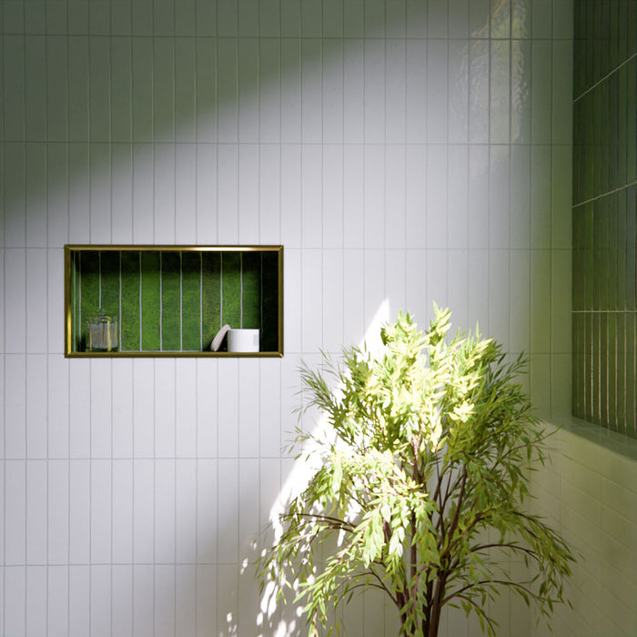 Modernes Badezimmer mit Bora Bora Ziegel Weißer Sand Keramik-Wandfliesen im schlanken Riemchenformat 6,5 × 32,8 cm mit Fluxglasur, vertikal und horizontal verlegt, um eine weich strukturierte Akzentwand zu schaffen. In Kombination mit freistehender Badewanne, Messingarmaturen, natürlichem Licht und Pflanzen entsteht eine ruhige, spaähnliche Atmosphäre.