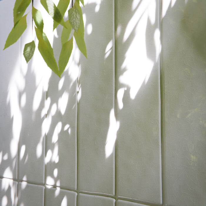 Modernes Badezimmer mit Bora Bora Ziegel Weißer Sand Keramik-Wandfliesen im schlanken Riemchenformat 6,5 × 32,8 cm mit Fluxglasur, vertikal und horizontal verlegt, um eine weich strukturierte Akzentwand zu schaffen. In Kombination mit freistehender Badewanne, Messingarmaturen, natürlichem Licht und Pflanzen entsteht eine ruhige, spaähnliche Atmosphäre.