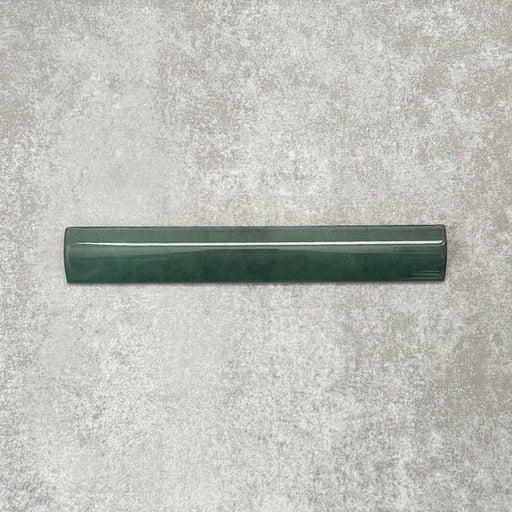 Zellige Königliches Grün Bordürenfliese Keramik-Abschlussfliese im marokkanischen Stil im Format 3 × 20 cm, in satten, tiefen Grüntönen. Die glatte, abgerundete Kante und die glänzende Glasur sind auf einem strukturierten grauen Hintergrund arrangiert und betonen die handwerkliche Zellige-Optik sowie das dekorative Kantenprofil.