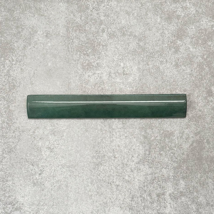 Zellige Königliches Grün Bordürenfliese Keramik-Abschlussfliese im marokkanischen Stil im Format 3 × 20 cm, in satten, tiefen Grüntönen. Die glatte, abgerundete Kante und die glänzende Glasur sind auf einem strukturierten grauen Hintergrund arrangiert und betonen die handwerkliche Zellige-Optik sowie das dekorative Kantenprofil.