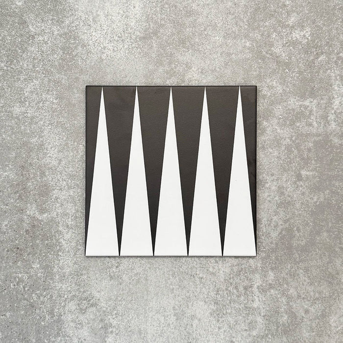 Schwarz-weiße Bodenfliese im Format 20x20 cm mit ausdrucksstarkem, geometrischem Muster im Backgammon-Stil. Markante Dreiecksformen treffen auf einen strukturierten grauen Hintergrund und schaffen eine klare, grafische Wirkung.