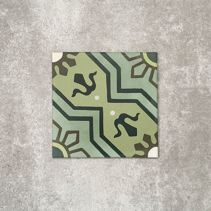 Einzelne Berlin Nikolai Feinsteinzeugfliese im Format 20 × 20 cm im marokkanisch inspirierten Stil vor einem neutralen Hintergrund in Steinoptik. Sichtbar ist ein detailreiches geometrisches Muster in abgestuften Grüntönen mit kontrastierenden dunklen Akzenten und matter Oberfläche im traditionell inspirierten Design.