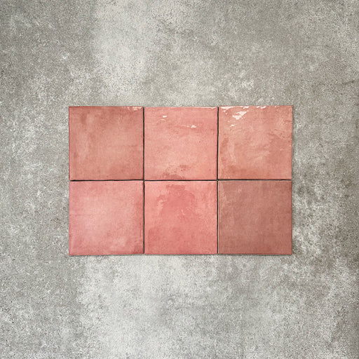 Flatlay von Zellige Rosa Quadrat Keramikfliesen im marokkanischen Stil im Format 13,2 × 13,2 cm, in sanften Blush-, Altrosa- und warmen Rosétönen. Dezente Farbnuancen und sanft unregelmäßige Kanten werden im schlichten Raster auf strukturiertem grauem Hintergrund gezeigt und betonen die handwerkliche Zellige-Oberfläche.