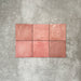 Flatlay von Zellige Rosa Quadrat Keramikfliesen im marokkanischen Stil im Format 13,2 × 13,2 cm, in sanften Blush-, Altrosa- und warmen Rosétönen. Dezente Farbnuancen und sanft unregelmäßige Kanten werden im schlichten Raster auf strukturiertem grauem Hintergrund gezeigt und betonen die handwerkliche Zellige-Oberfläche.