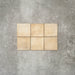 Flat lay of Zellige Arena Marfil Square 10 × 10cm Moroccan-style ceramic tiles in warm beige and sand hues, displaying subtle shade variation and softly uneven edges, arranged in a simple grid on a textured grey background to showcase the handcrafted zellige-effect surface.