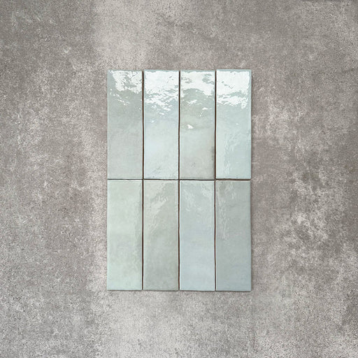 Flatlay von Zellige Aquablau Keramik-Riemchenfliesen im marokkanischen Stil im Format 6,5 × 20 cm, mit sanften Blau-Grün-Tönen, glänzender Glasur in Handarbeit-Optik und feiner tonaler Variation vor neutralem Hintergrund.