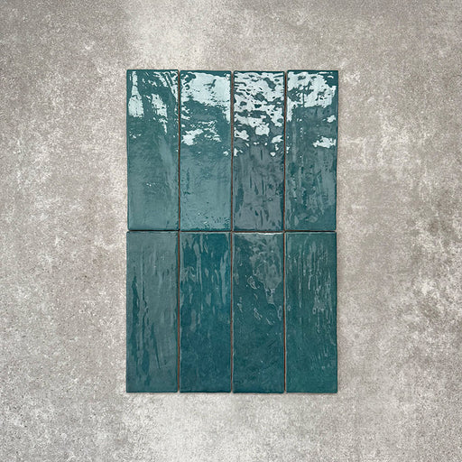 Flatlay von Zellige Pfauengrün Keramik-Ziegelfliesen im marokkanischen Stil im Format 6,5 × 20 cm, mit satten Blau-Grün-Tönen, glänzender Glasur in handgefertigter Optik und natürlicher Farbvariation auf neutralem Hintergrund.