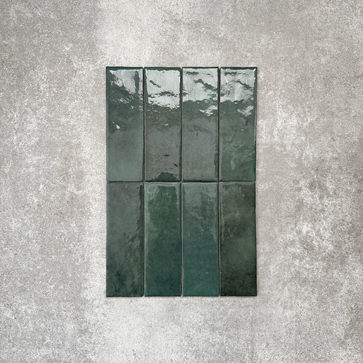 Flatlay von Zellige Königliches Grün Ziegel Keramikfliesen im marokkanischen Stil im Format 6,5 × 20 cm, in satten, tiefen Grüntönen. Vertikal im Ziegelverband auf strukturiertem grauem Hintergrund arrangiert, um die glänzende Glasur, natürliche Farbvariation und die handgefertigte Zellige-Optik zu zeigen.