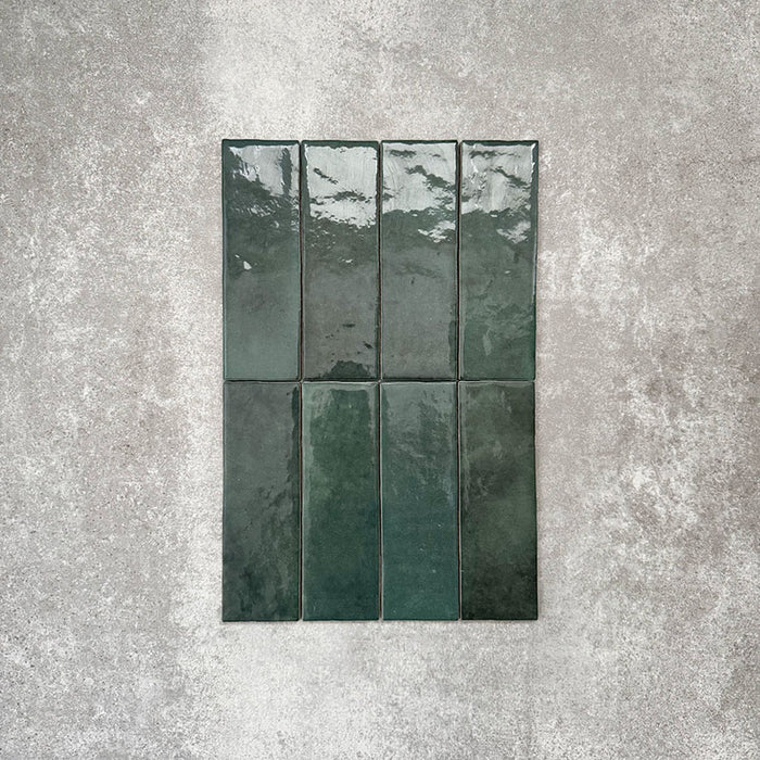 Flatlay von Zellige Königliches Grün Ziegel Keramikfliesen im marokkanischen Stil im Format 6,5 × 20 cm, in satten, tiefen Grüntönen. Vertikal im Ziegelverband auf strukturiertem grauem Hintergrund arrangiert, um die glänzende Glasur, natürliche Farbvariation und die handgefertigte Zellige-Optik zu zeigen.