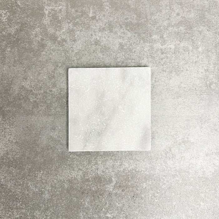 Einzelne Fayrouz White 15,2 × 15,2 cm Naturmarmorfliese mit getrommelter Oberfläche in sanften Weißtönen mit dezenter natürlicher Maserung, präsentiert vor einem neutralen, strukturierten Hintergrund in einer klaren Produktszene.