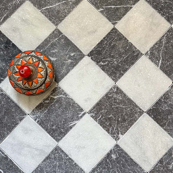Schachbrettmuster mit Fayrouz White 15,2 × 15,2 cm Naturmarmorfliesen mit getrommelter Oberfläche, kombiniert mit schwarzen Marmorfliesen, diagonal verlegt und mit einer dekorativen Schale für zusätzlichen visuellen Kontrast inszeniert.